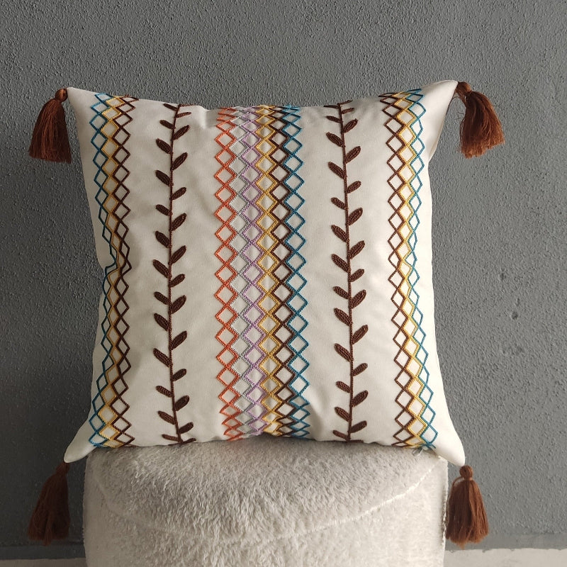 Square boho cushion cover with multi-color embroidered geometric and leaf pattern, finished with brown tassels on all four corners, 43x43 cm
