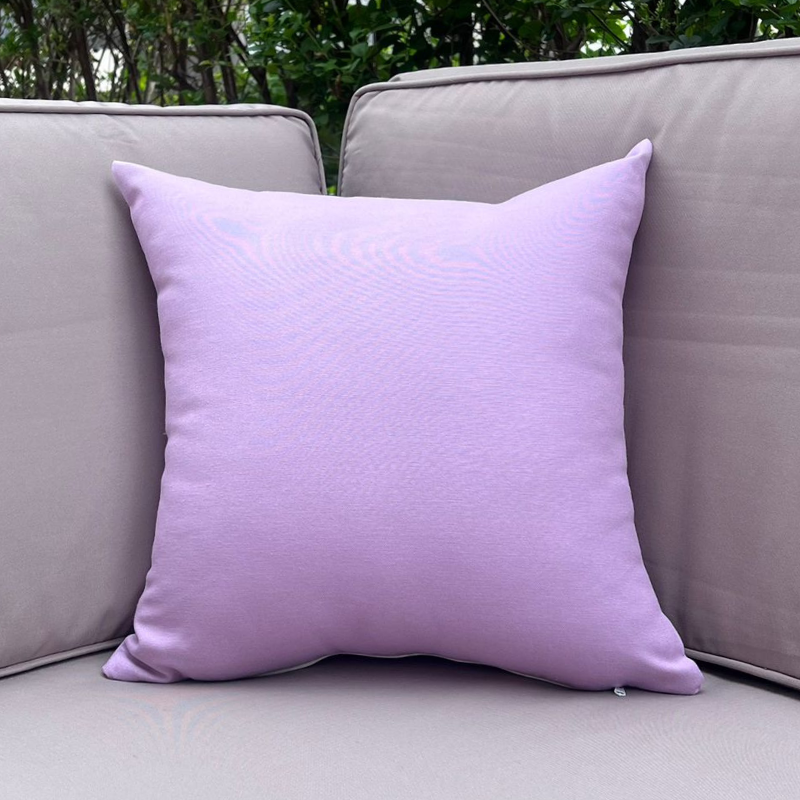 Lavender cushion cover displayed on a beige outdoor sofa in a garden patio setting