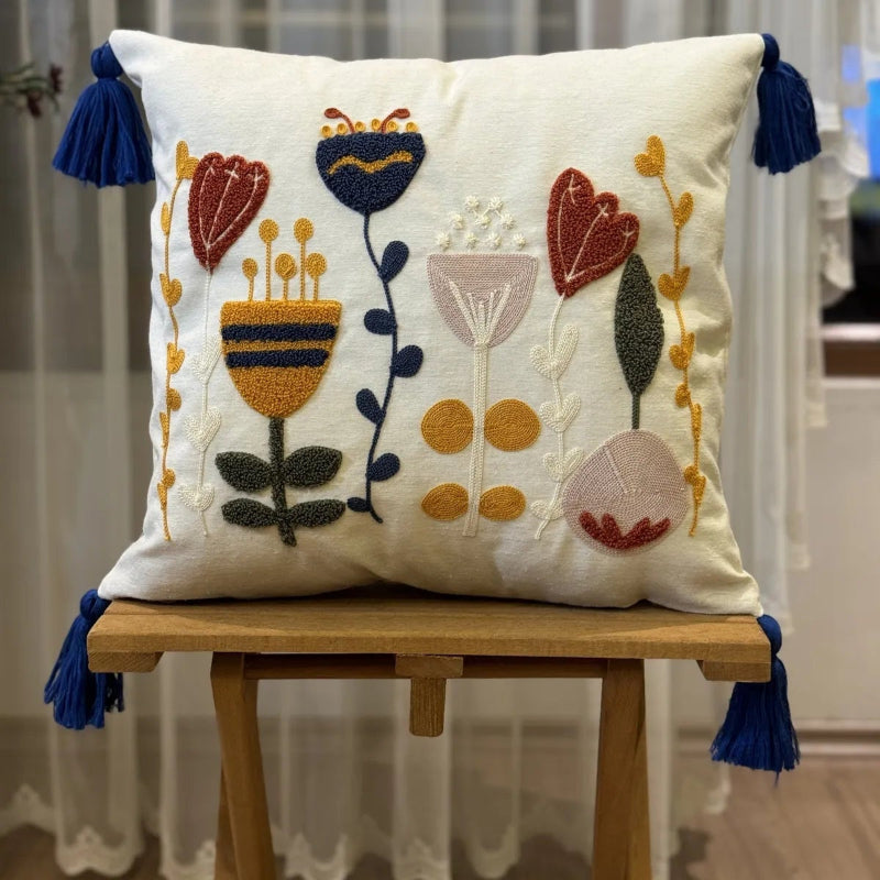 Boho embroidered floral cushion cover with colorful folk-inspired flowers and blue tassels on an ivory cotton base placed on outdoor grey sofa