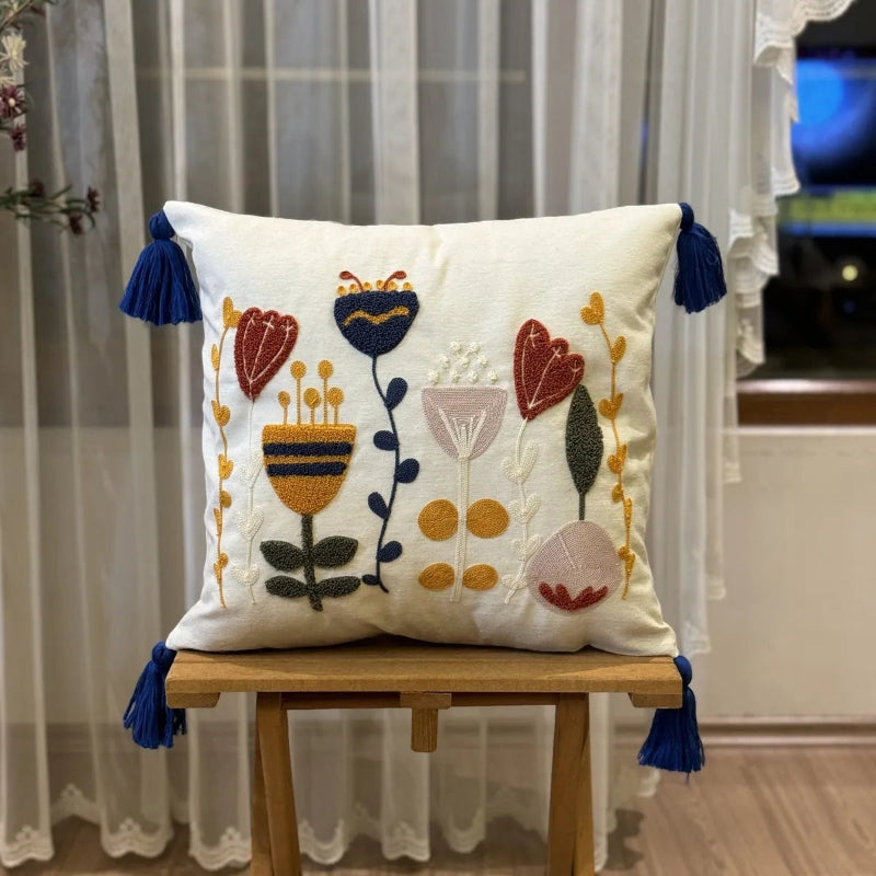 Boho embroidered floral cushion cover with colorful folk-inspired flowers and blue tassels on an ivory cotton base placed on outdoor grey sofa