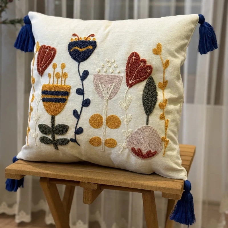 Boho embroidered floral cushion cover with colorful folk-inspired flowers and blue tassels on an ivory cotton base placed on outdoor grey sofa
