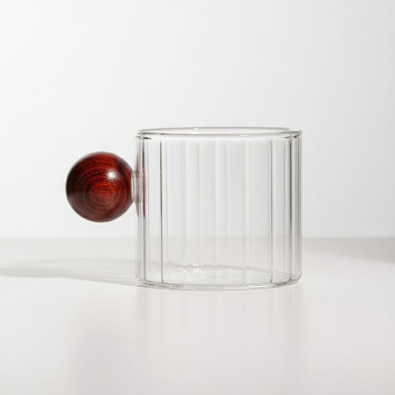 Ribbed glass mug with wooden ball handle on white background
Modern artistic coffee cup with ribbed glass body
Transparent glass mug with unique round wooden handle
Designer borosilicate glass mug for coffee or tea