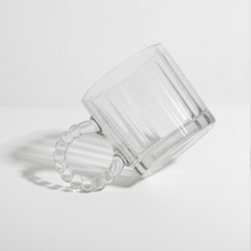 Clear ribbed glass mug with beaded handle on white background
Vintage-style glass coffee cup with decorative handle
Transparent ribbed mug for coffee, tea, or juice
Artistic clear glass mug with round beaded handle