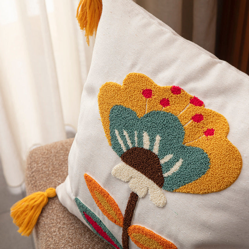 Cream cushion cover with tufted floral embroidery in mustard, teal, red, and yellow tassels