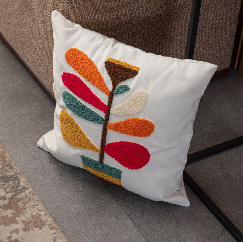 Cream cushion cover with colorful tufted leaf embroidery and yellow tassels on each corner