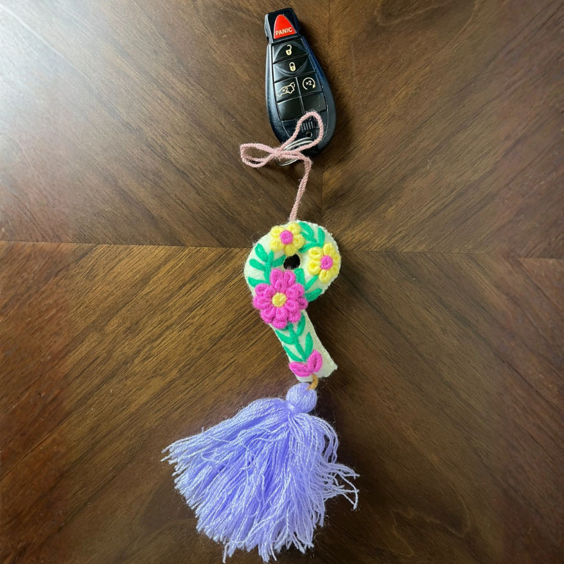 Handmade embroidered letter P ornament with colorful floral embroidery and lavender tassel on wooden background