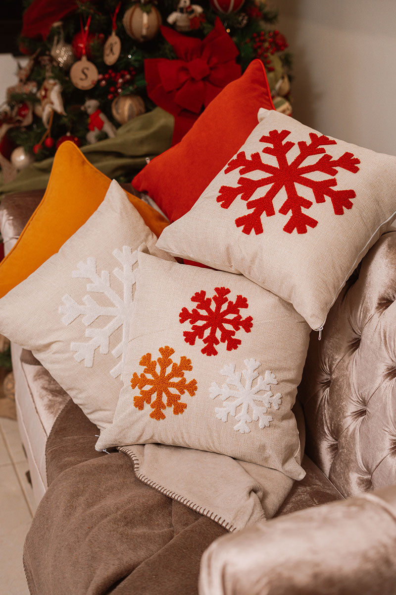Beige cushion with embroidered snowflakes in white, red, and orange on a blue sofa – Autumn Bloom Collection