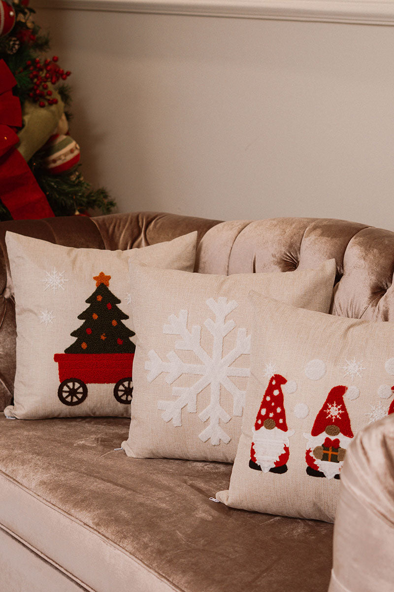Beige cushion with embroidered red wagon carrying a Christmas tree topped with a gold star on a blue sofa – Autumn Bloom Collection