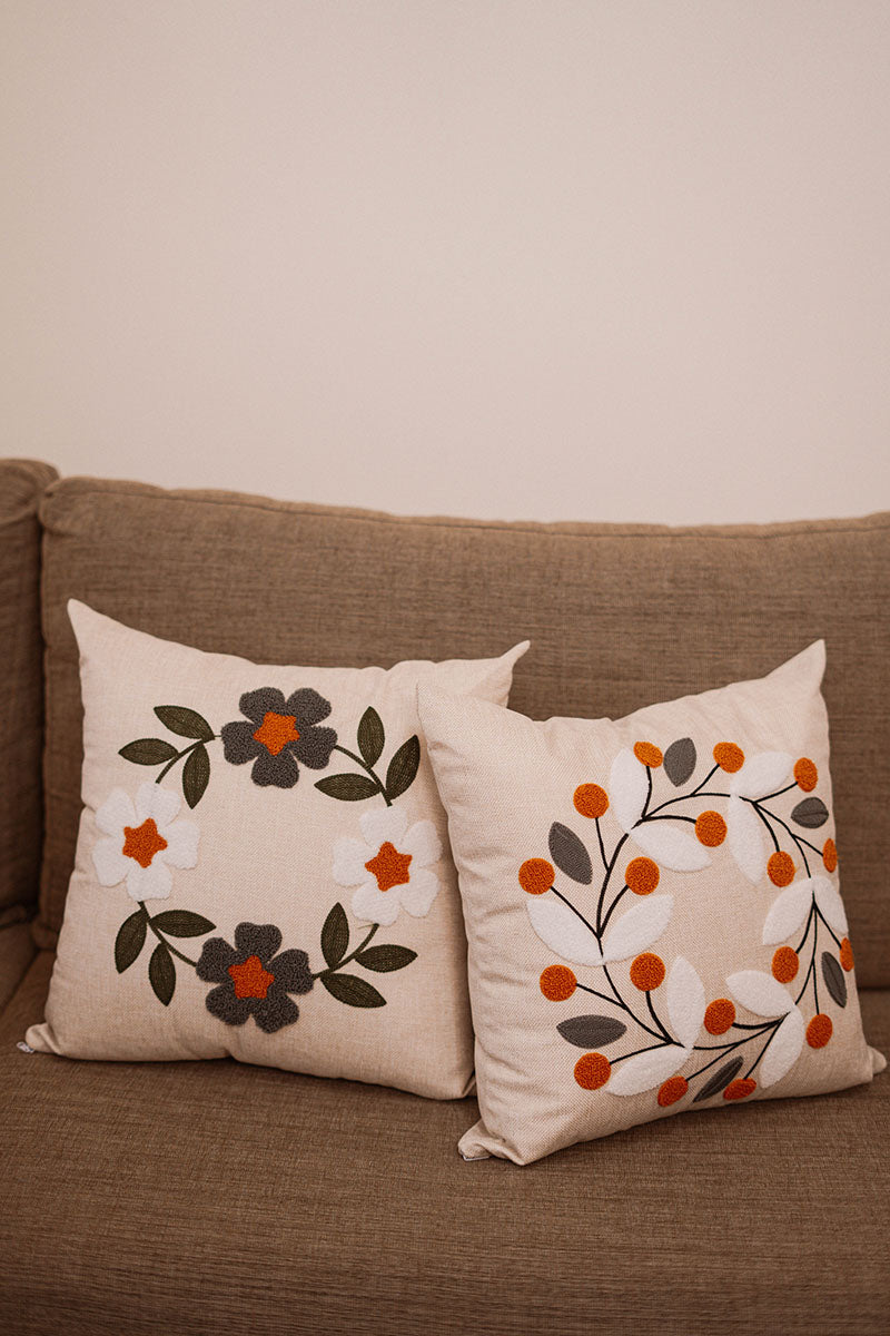 Hand-embroidered cushion with blue and rust flowers on beige fabric, placed on a blue sofa