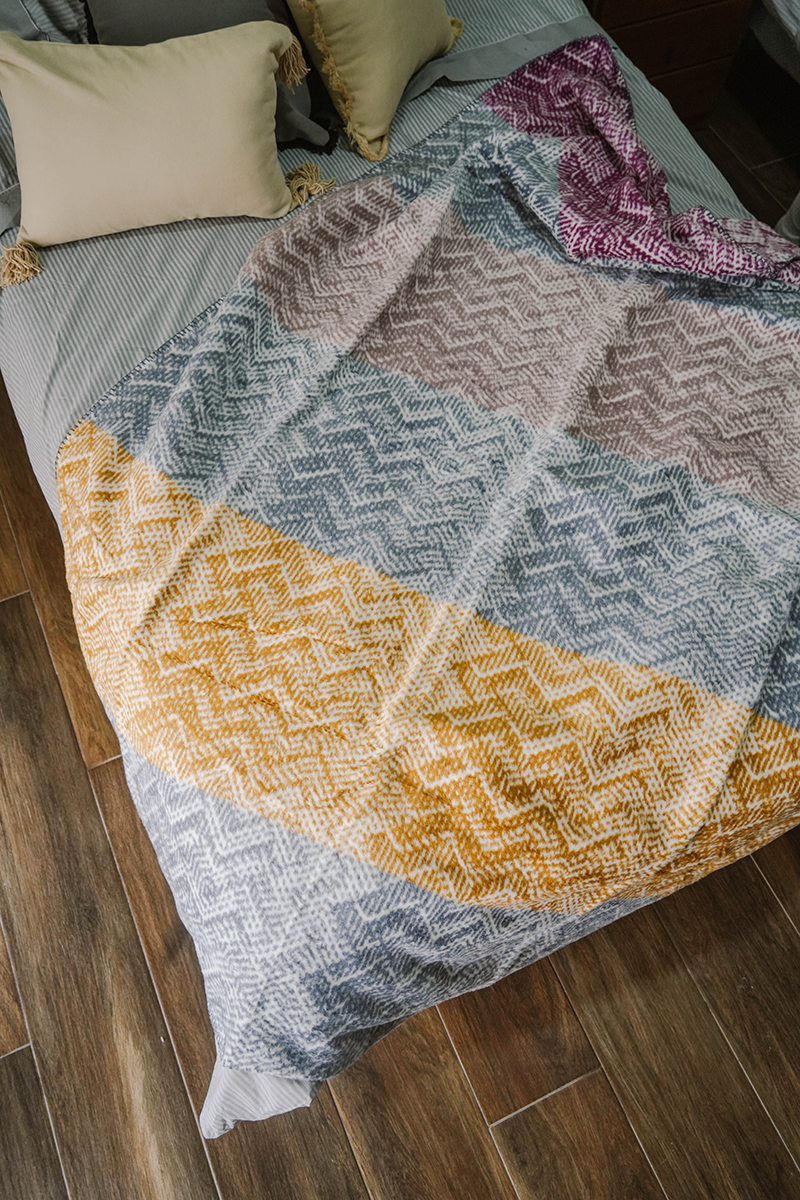 Multicolor chevron fleece blanket in yellow, purple, pink, and grey on sofa