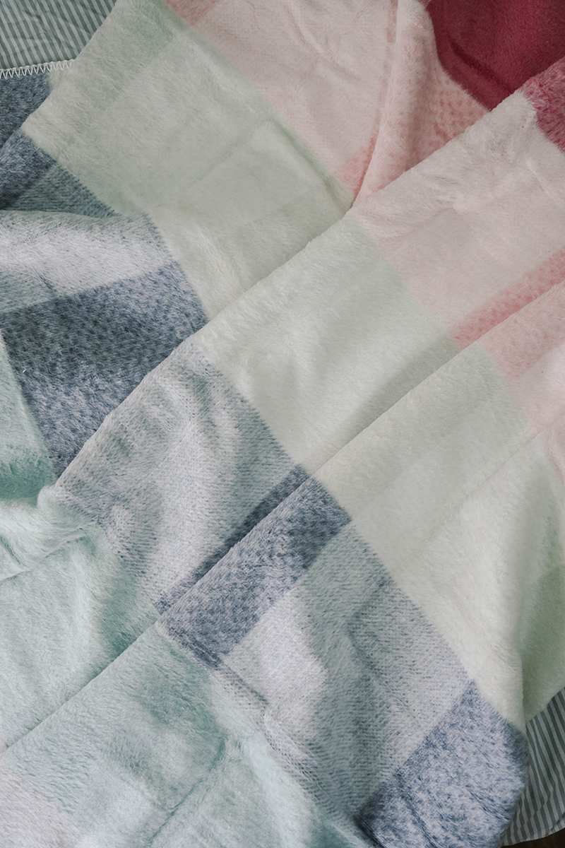Pastel checkered fleece blanket in pink, grey, aqua, and white draped on ladder