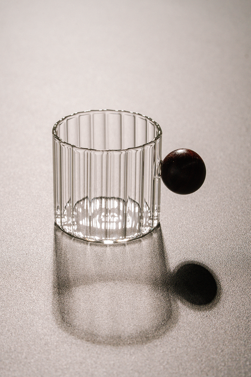 Ribbed glass mug with wooden ball handle on white background
Modern artistic coffee cup with ribbed glass body
Transparent glass mug with unique round wooden handle
Designer borosilicate glass mug for coffee or tea