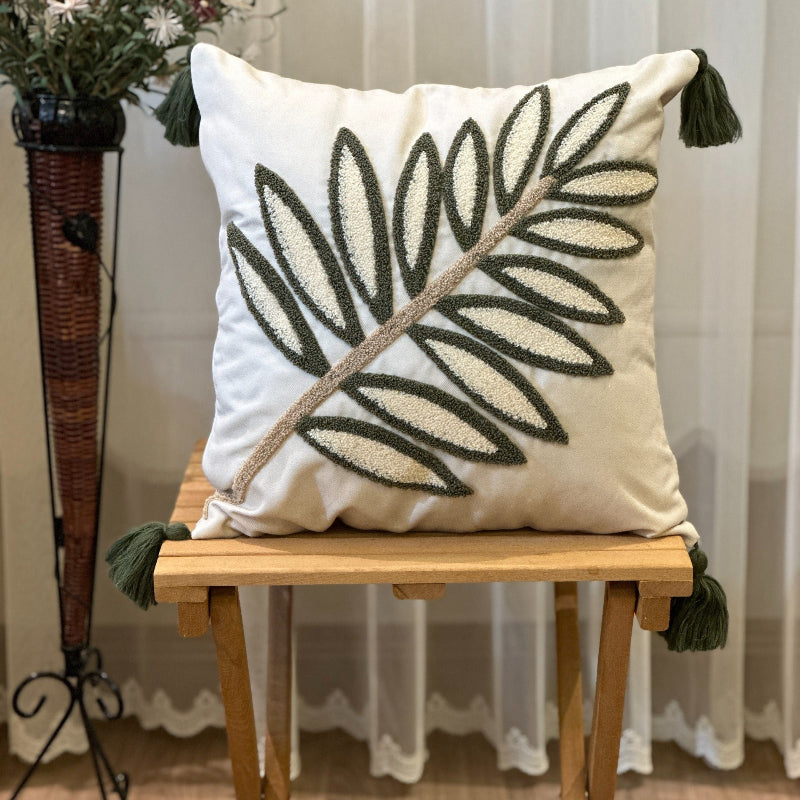Handcrafted decorative throw pillow with green leaf embroidery and tassels on a wooden table