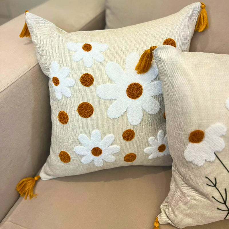 Square embroidered daisy cushion cover with mustard accents and tassels on beige sofa