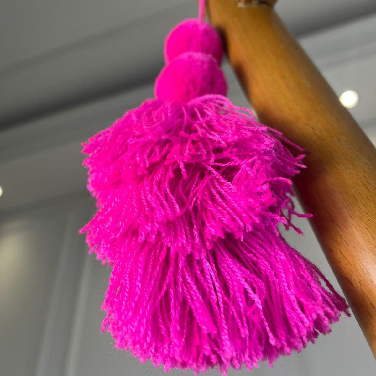 Hot pink pom-pom tassel hanging decoration with two pom-poms and layered pink yarn tassels hanging on a wooden chair.