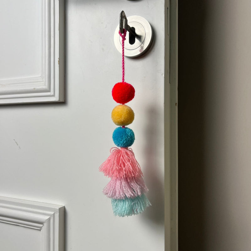 Handmade pom pom tassel hanging decor with colorful pom poms and layered pastel yarn tassels on white door background