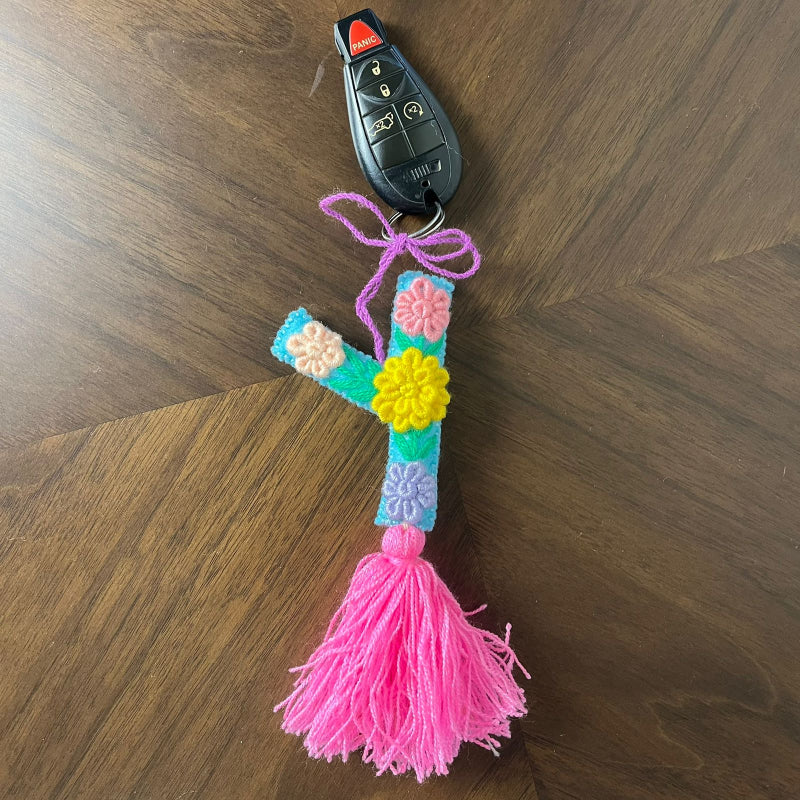 Handmade embroidered letter Y ornament with colorful floral stitching and bright pink tassel on wooden surface