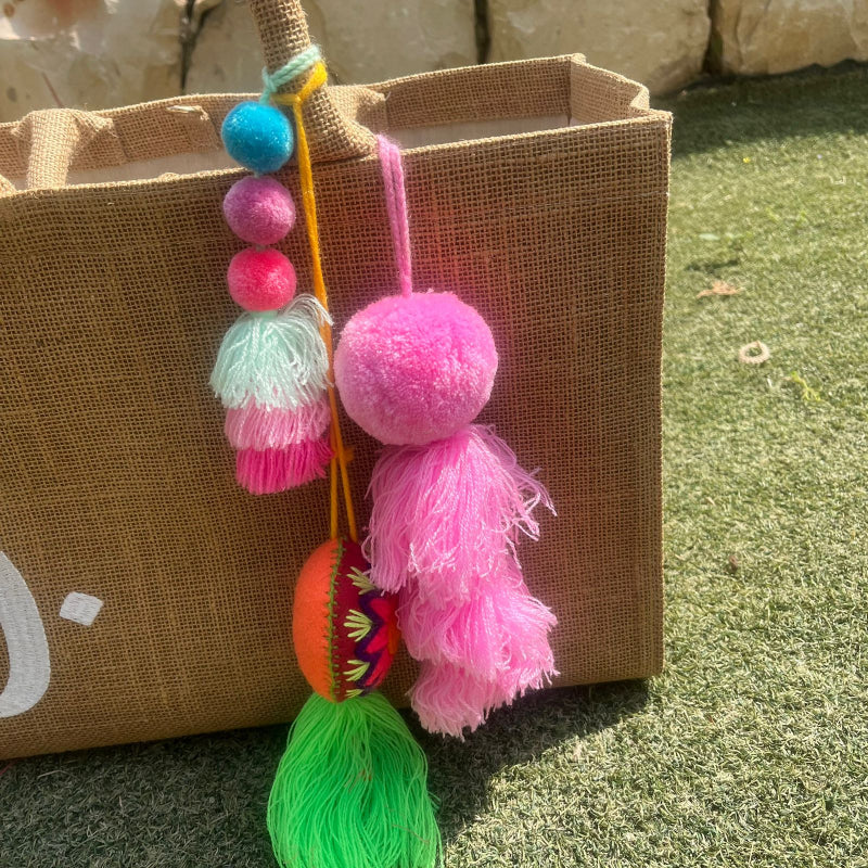 Pink fluffy tassel keychain with soft pom pom placed on grass background