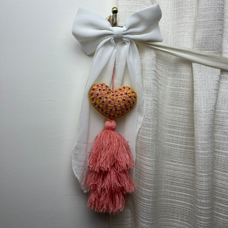 Handmade embroidered heart tassel with pink yarn fringe hanging on curtain