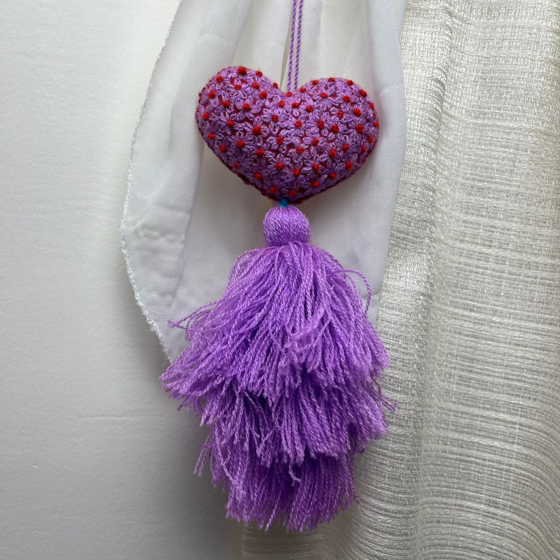 Handmade purple embroidered heart tassel with red floral embroidery and purple yarn fringe on curtain
