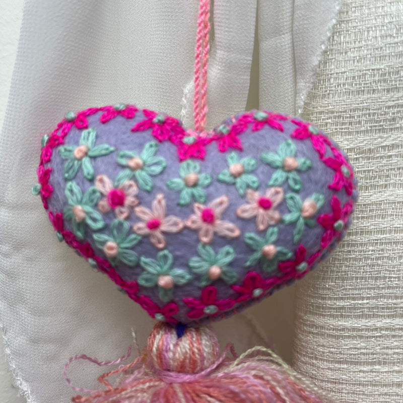 Handmade lavender embroidered heart tassel with colorful floral embroidery and pink yarn fringe on curtain