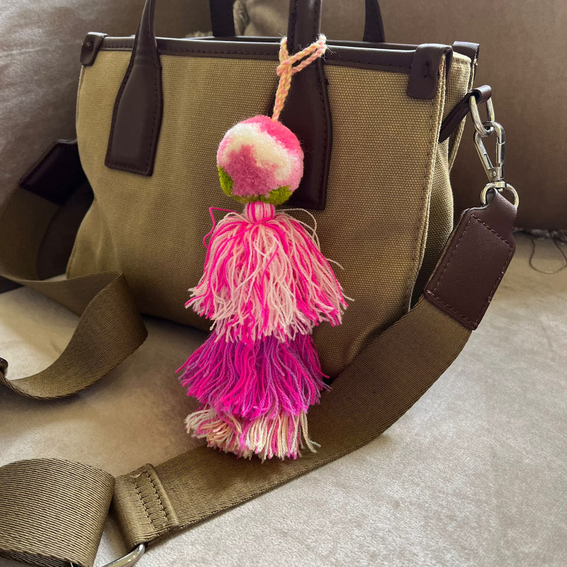 Blush pink pom pom tassel bag charm with layered pink tassels attached to a beige handbag