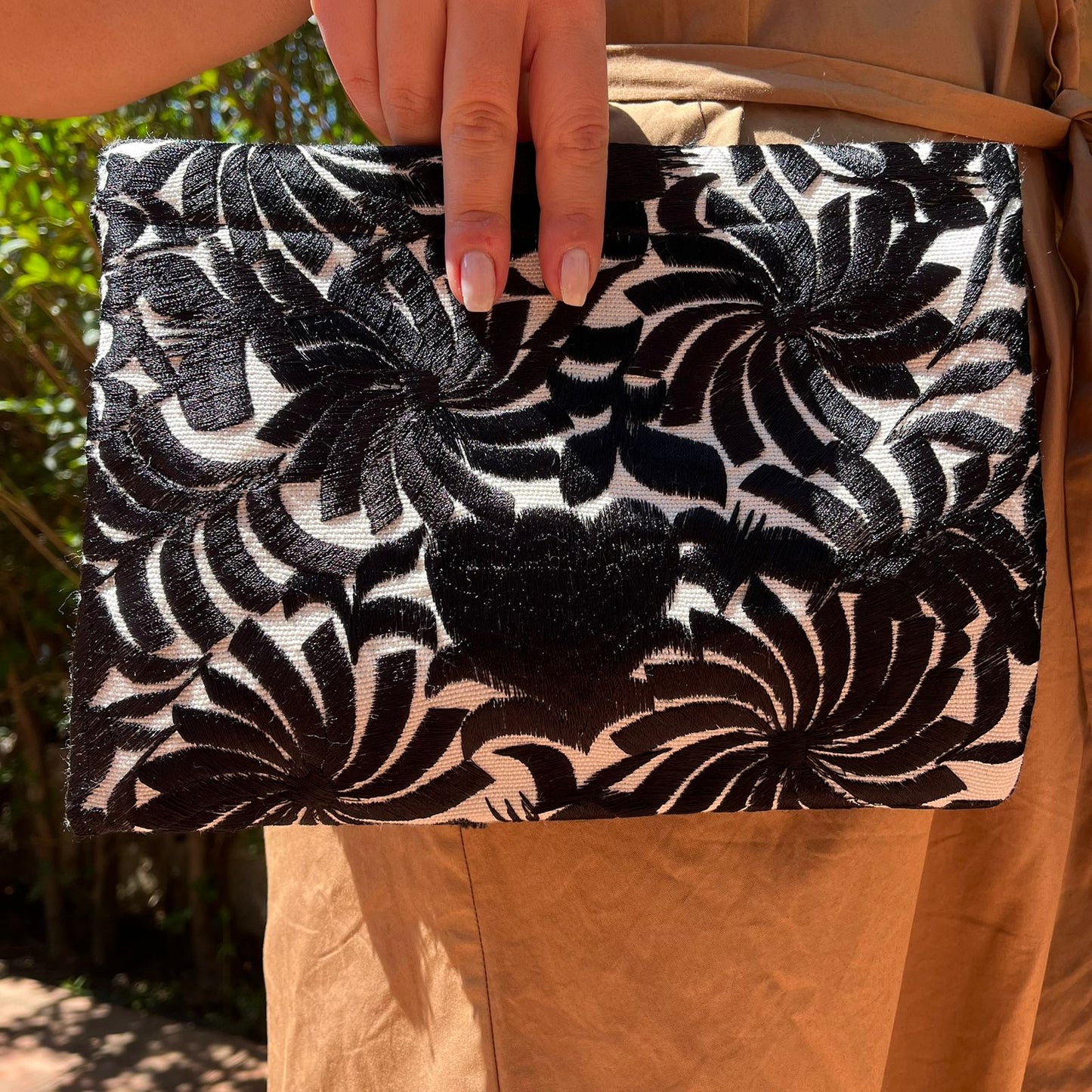 Woman holding a black and white embroidered clutch with tassels in a monochrome boho style outdoors