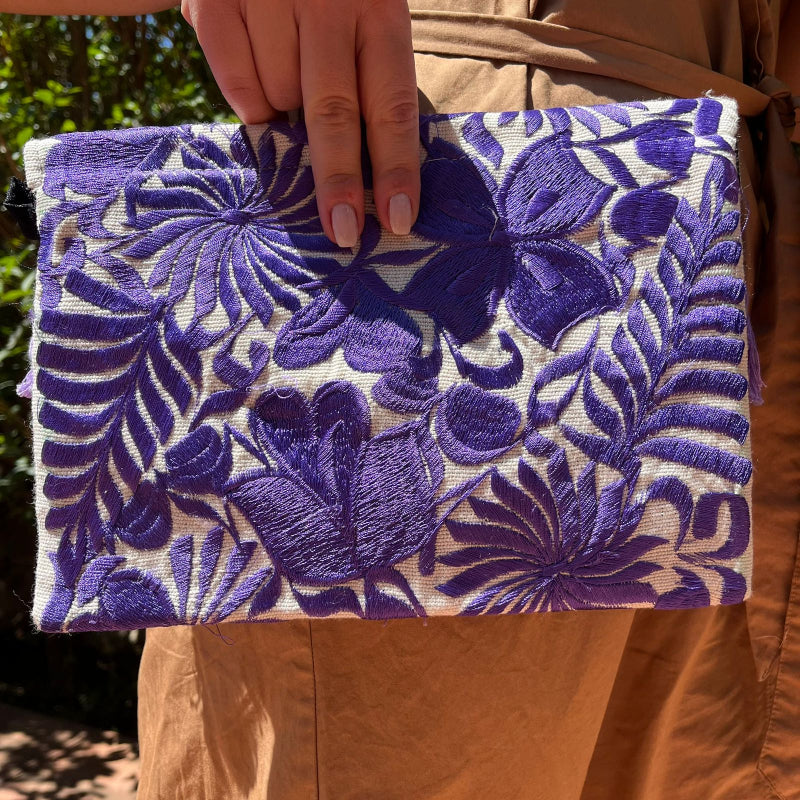 Purple floral embroidered clutch bag with tassels held by a person wearing a brown dress outdoors