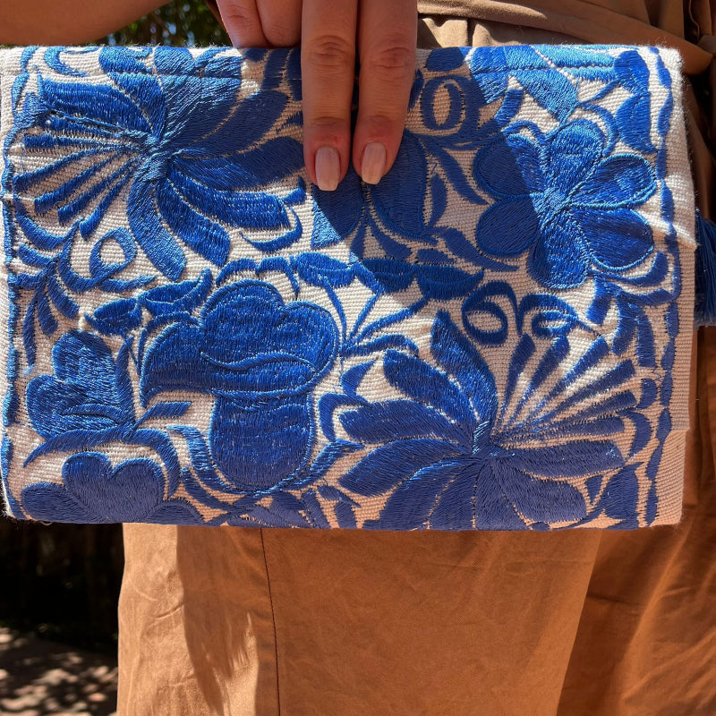 Blue floral embroidered clutch bag with tassels held by a person wearing a brown dress outdoors