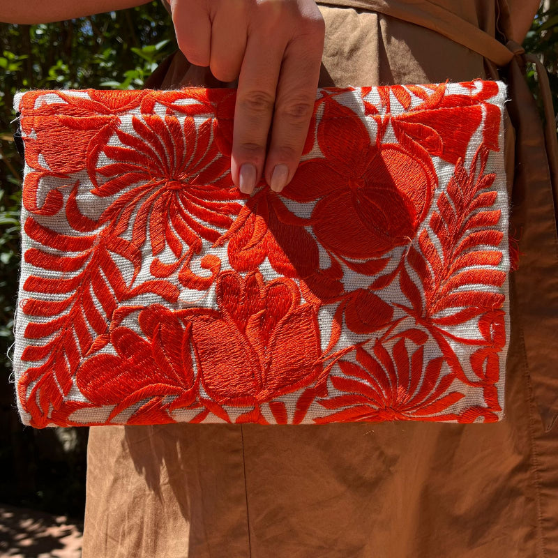 Red floral embroidered clutch bag with tassels held by a person wearing a brown dress outdoors