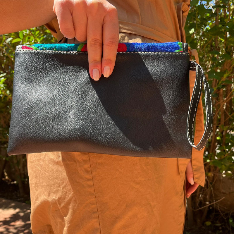 Woman wearing a black leather shoulder bag with colorful floral embroidered flap outdoors
