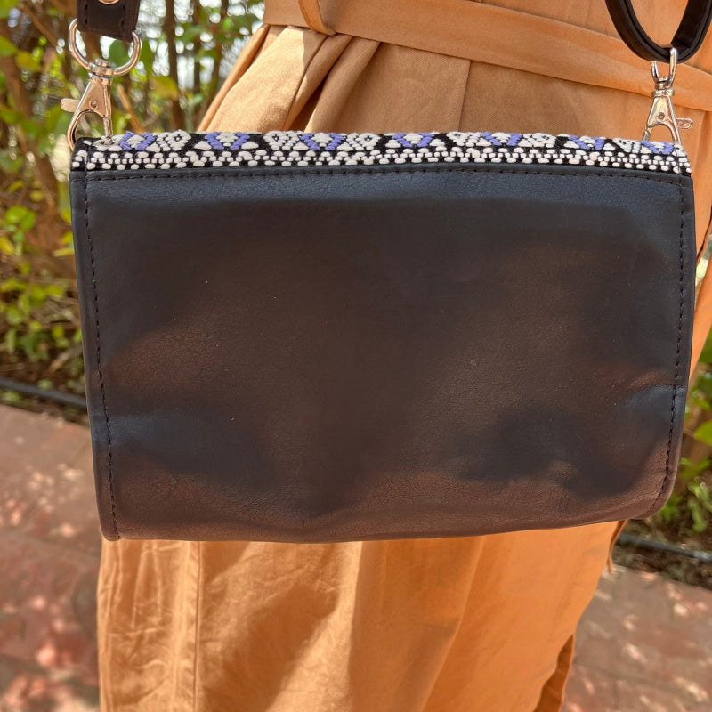 Handcrafted black leather crossbody bag with geometric woven flap worn outdoors