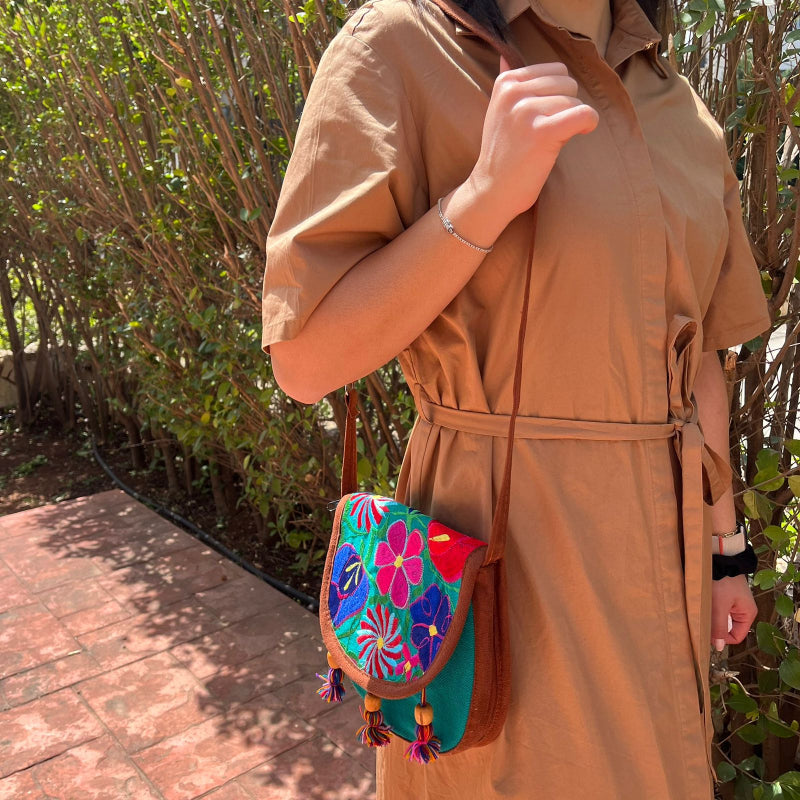 Close-up of a turquoise crossbody bag with colorful floral embroidery and tassels worn outdoors