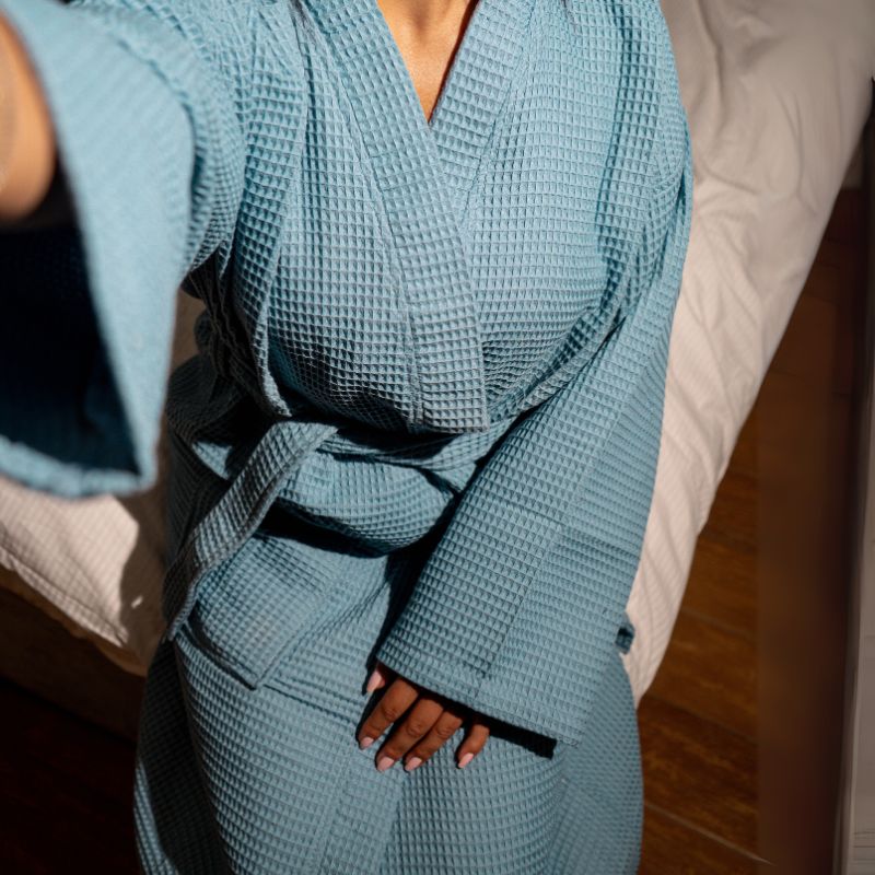 Blue waffle cotton bathrobe with belt and front pockets worn by woman on a balcony