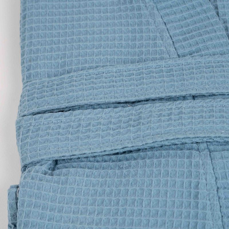 Blue waffle cotton bathrobe with belt and front pockets worn by woman on a balcony
