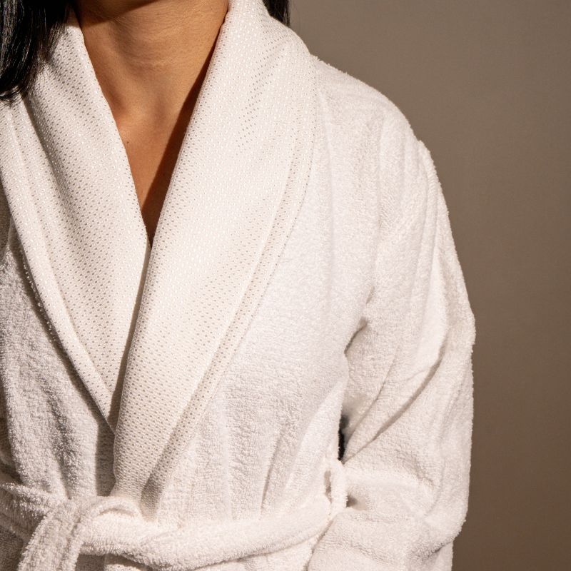 Unisex cotton terry bathrobe with shawl collar and waist belt, worn by woman near window in natural light