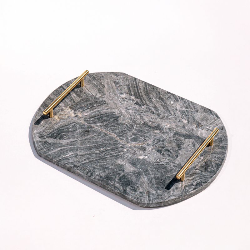 dark grey oval capsule-shaped marble tray with brass handles placed by the pool