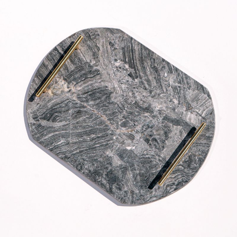 dark grey oval capsule-shaped marble tray with brass handles placed by the pool