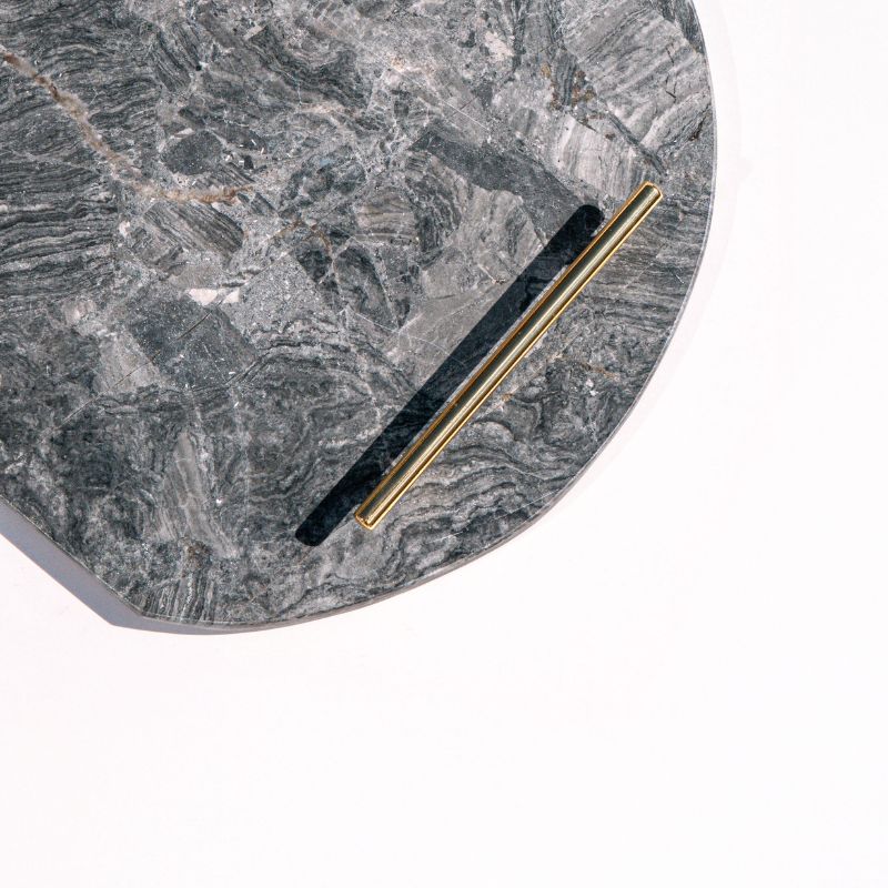 dark grey oval capsule-shaped marble tray with brass handles placed by the pool