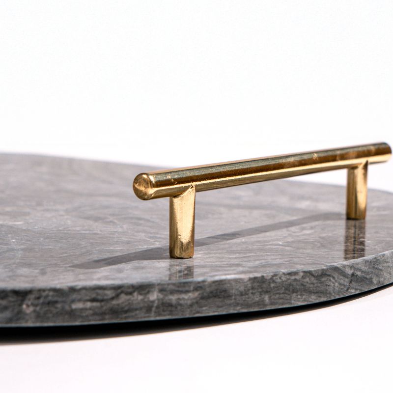 dark grey oval capsule-shaped marble tray with brass handles placed by the pool