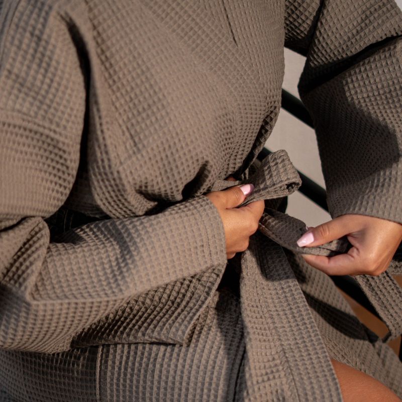 Greige waffle cotton bathrobe with belt and front pockets worn by woman on a balcony