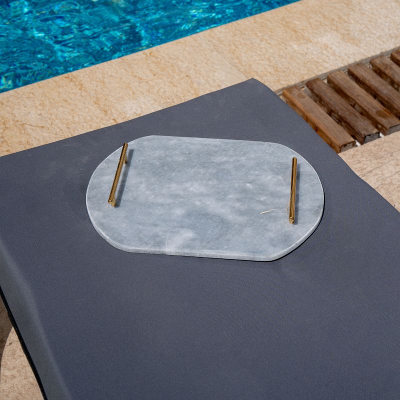 Light grey oval capsule-shaped marble tray with brass handles placed by the pool