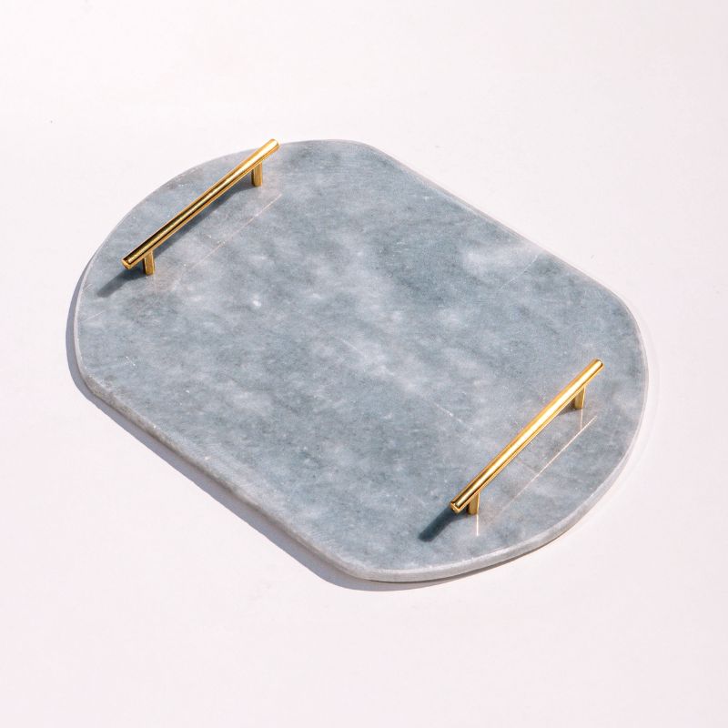Light grey oval capsule-shaped marble tray with brass handles placed by the pool