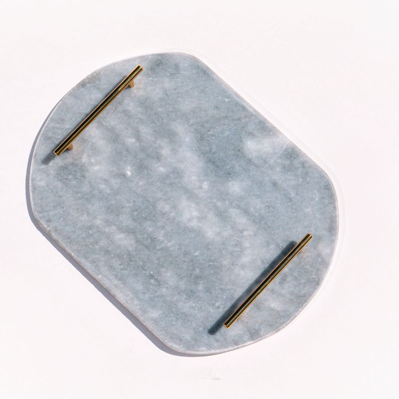 Light grey oval capsule-shaped marble tray with brass handles placed by the pool