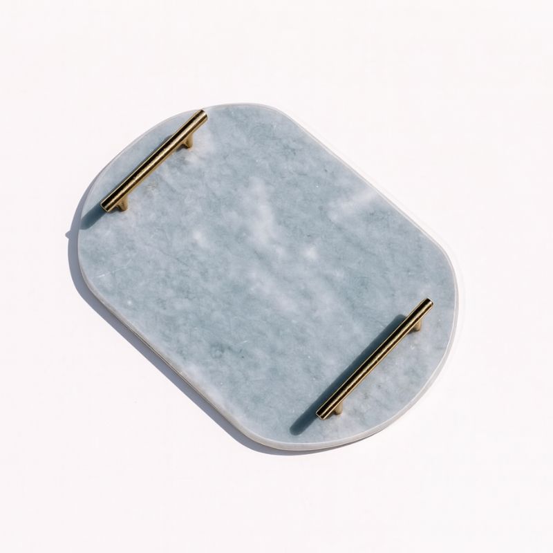 Light grey oval capsule-shaped marble tray with brass handles placed by the pool