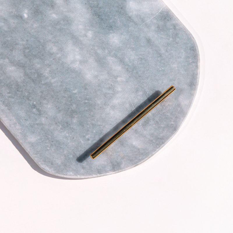 Light grey oval capsule-shaped marble tray with brass handles placed by the pool