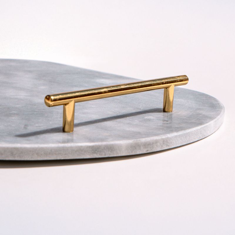 Light grey oval capsule-shaped marble tray with brass handles placed by the pool