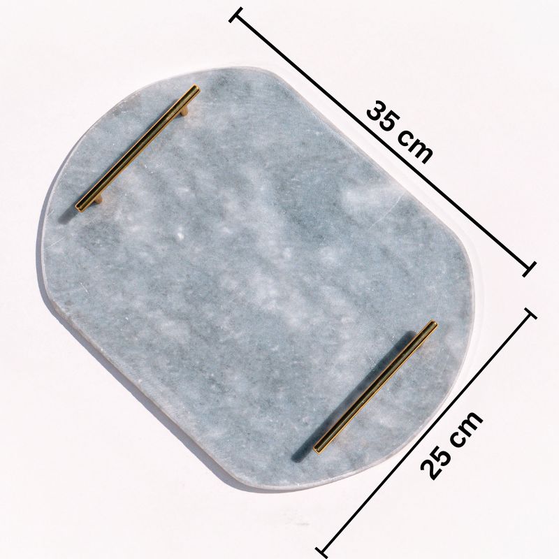 Light grey oval capsule-shaped marble tray with brass handles placed by the pool