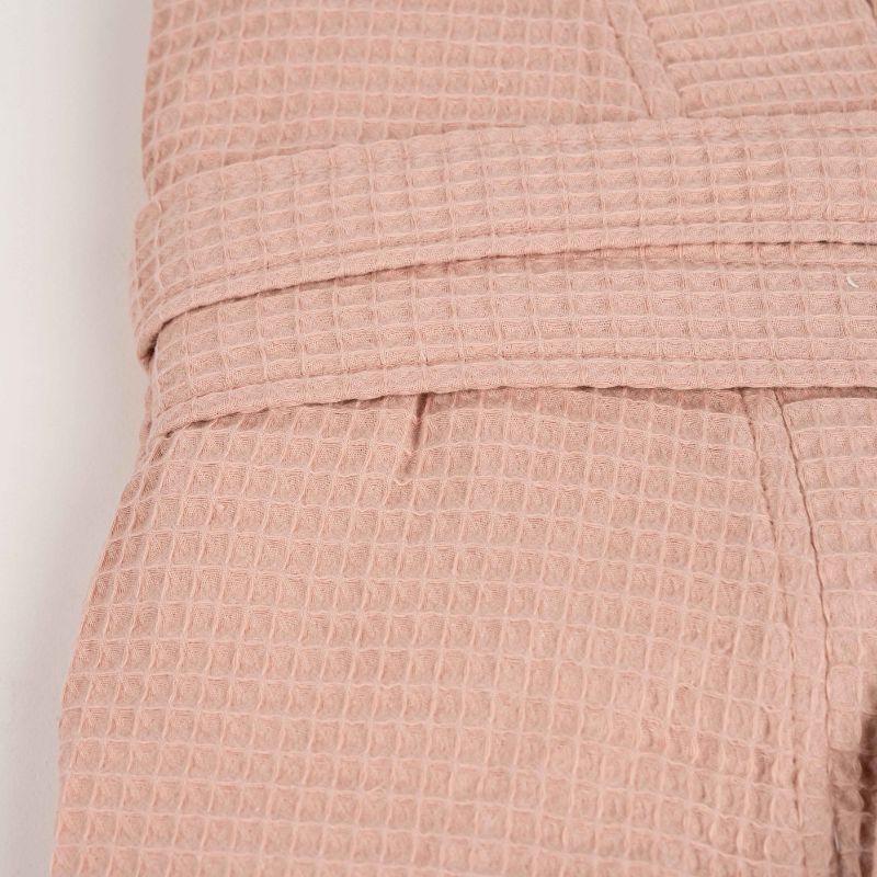 Pink waffle cotton bathrobe with belt and front pockets worn by woman on a balcony