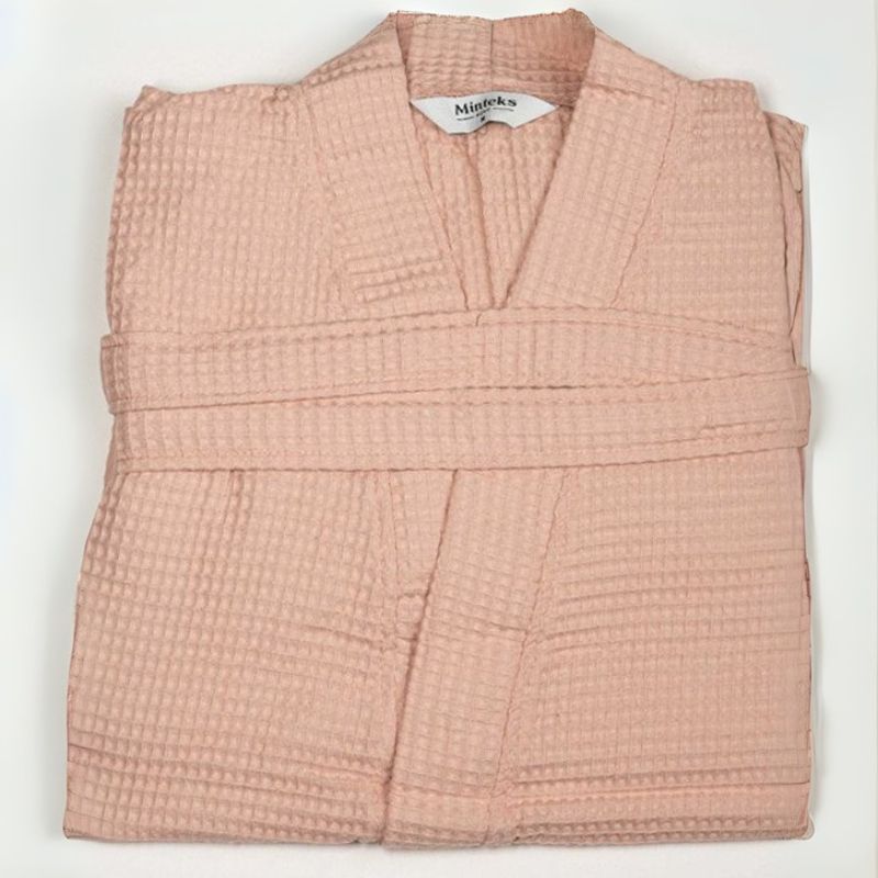 Pink waffle cotton bathrobe with belt and front pockets worn by woman on a balcony